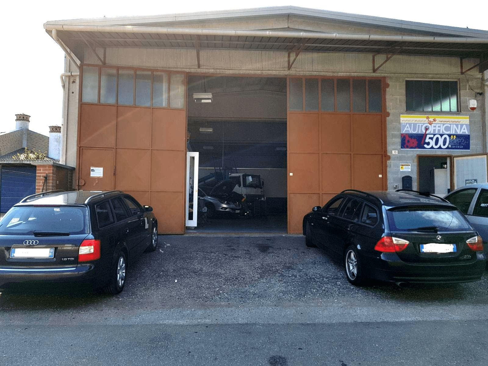 Capannone di Officina 500 in Via Monte Rosa 13 con portone aperto e insegna Autofficina 500